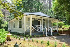 A small, single-story building with a porch, surrounded by a garden and trees. - Franklin Cottage (Olinda)
