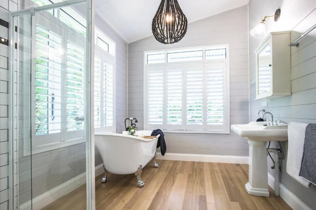 A bathroom with a freestanding bathtub, a pedestal sink, and a large window with shutters.