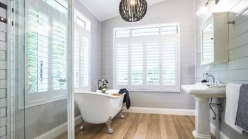 A bathroom with a freestanding bathtub, a pedestal sink, and a large window with shutters.