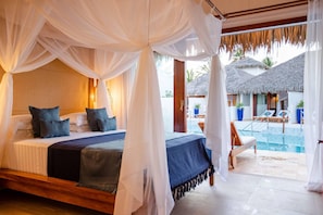 Ein Schlafzimmer mit Baldachinbett, Blick auf einen Pool und einem Reetdachgebäude.
