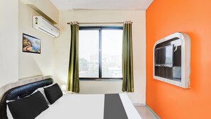 Ein Hotelzimmer mit einem Bett, einem Vorhangfenster, einer Klimaanlage, einem Wandbild und einem an der Wand befestigten Fernseher.