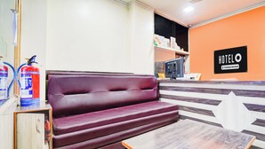 Ein Hotel-Empfangsbereich mit einer Rezeption, einem violetten Sofa, einem kleinen Tisch und einem Feuerlöscher.