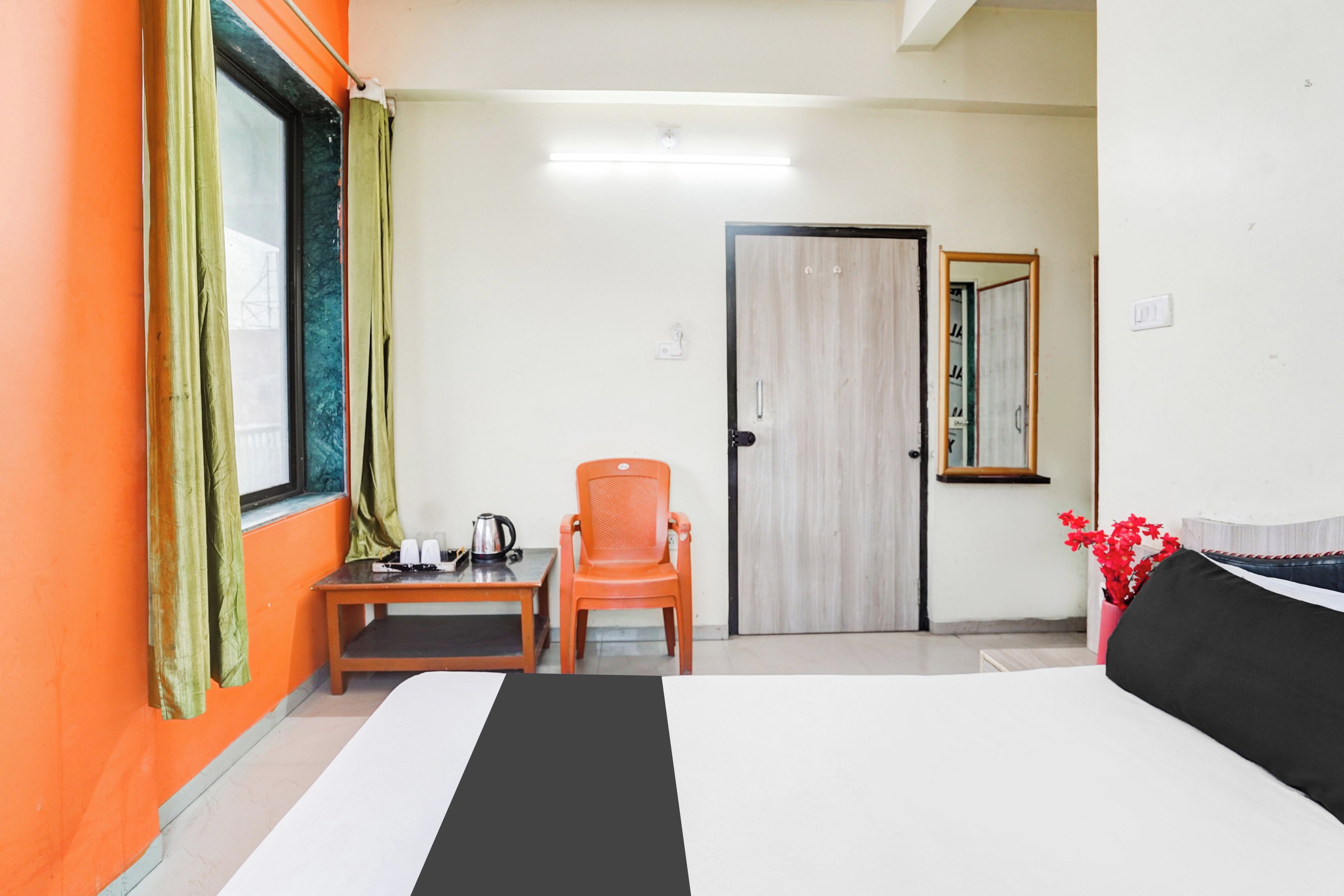 Hotellihuone, jossa on sänky, pieni pöytä, jossa on vedenkeitin, tuoli ja ovi.