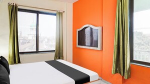 Ein Hotelzimmer mit einem Bett, einem Fenster mit Vorhängen und einer orangefarbenen Wand.