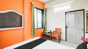 Ein Zimmer mit einem Bett, einem Tisch mit Wasserkocher, einem Stuhl und einer Tür.