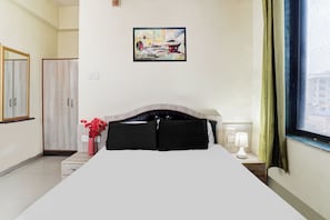 Habitació d'hotel amb un llit, una taula de nit, una làmpada, un vas amb flors, un quadre a la paret i una finestra amb cortines.
