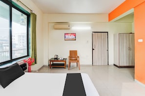 Een hotelkamer met een bed, een stoel, een tafel met een waterkoker, een schilderij en een kast.