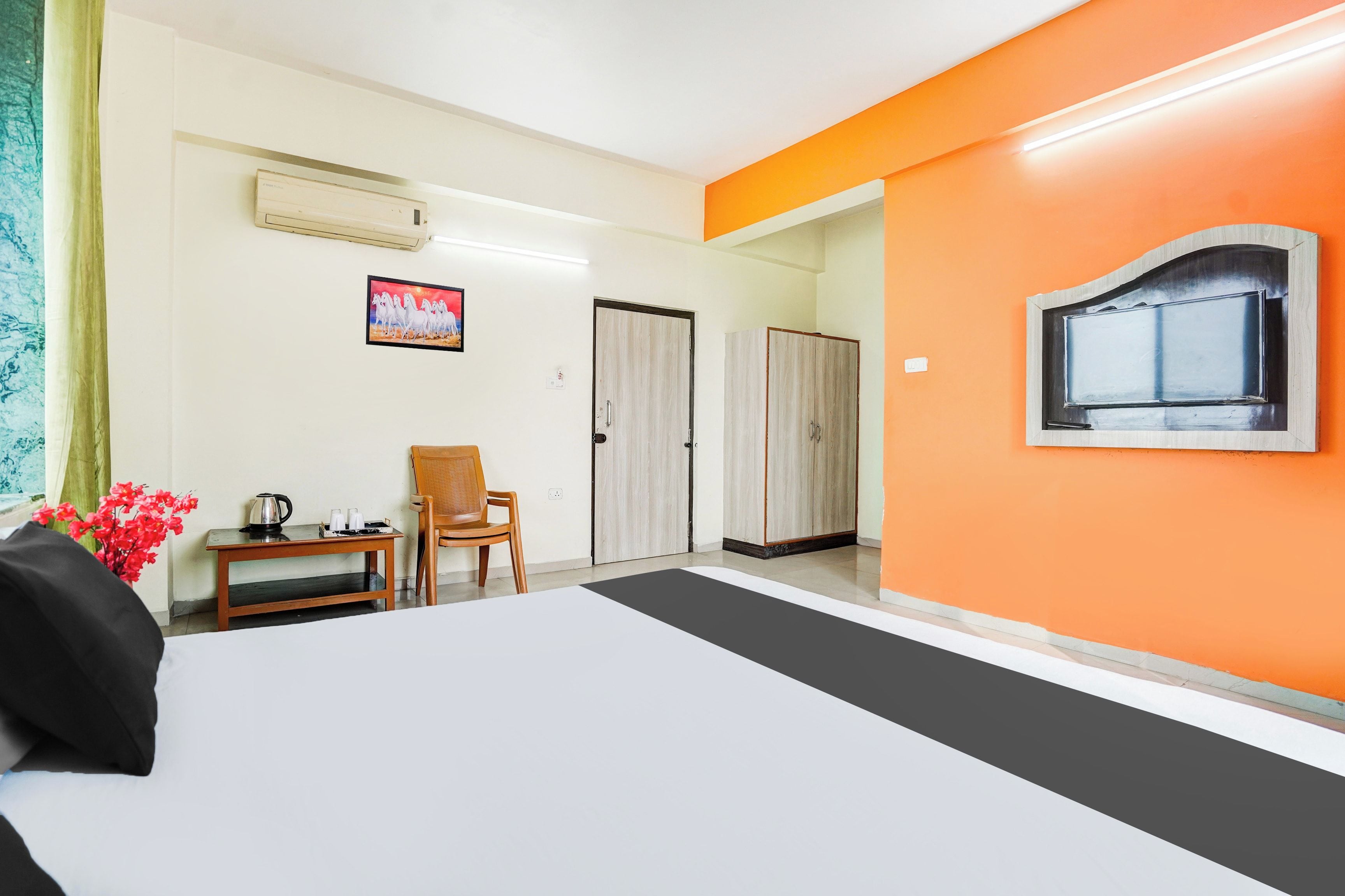Une chambre d’hôtel avec un lit, une chaise, une table avec une bouilloire, un tableau au mur et un appareil de climatisation.