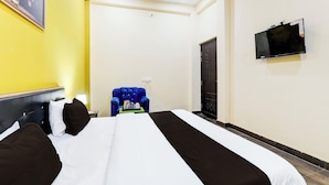 Una habitación de hotel con una cama, un sillón azul, un televisor y una puerta.