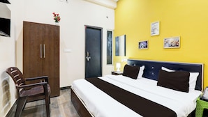 Habitación de hotel con cama, una silla, armario, puerta y pared decorada con cuadros.