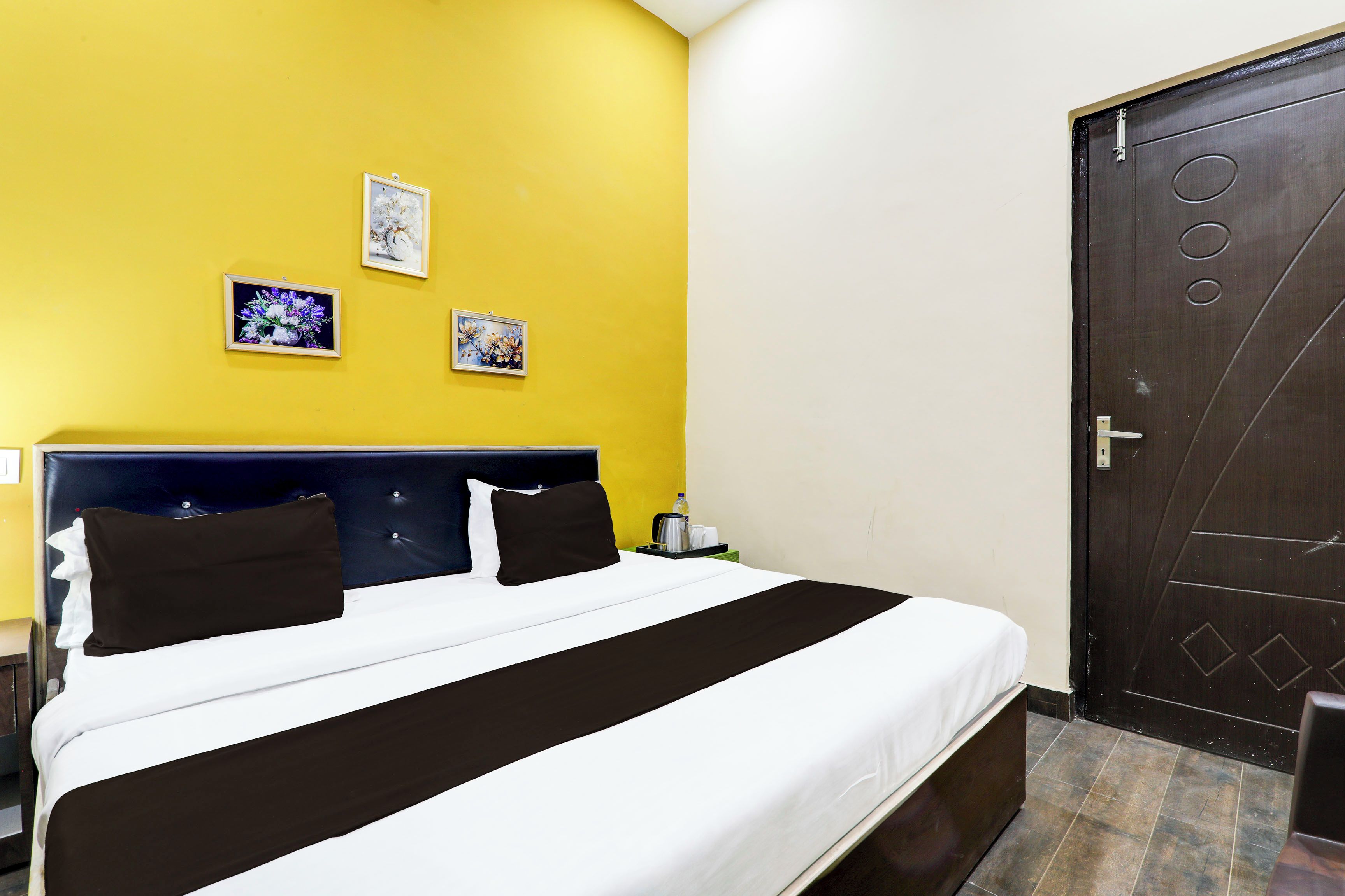 A hotel room with a bed, a nightstand, a door, and three framed pictures on the wall.