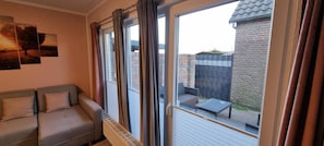 Quarto com sofá, janela com cortinas e vista para uma parede de tijolos e uma cerca de metal lá fora.