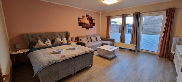 Quarto de hotel com cama, sofá, mesa de centro e janela com cortinas.