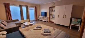 Quarto de hotel com sofá, cama com colcha, televisão, armário e janela com cortinas.