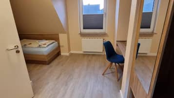 Eine kleine Einzimmerwohnung mit schrägem Dach, einem Bett, einem Sessel und zwei Fenstern.