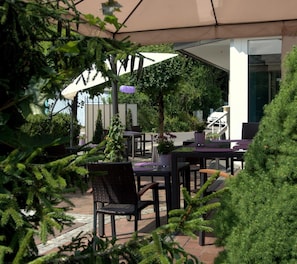 An outdoor seating area with tables and chairs, surrounded by greenery and a covered structure. - Best Breakfast - Hotel Justina (Bad Woerishofen)