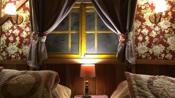 Una habitación con dos camas, una mesita de noche con lámpara y una ventana con cortinas.