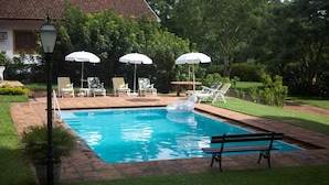 A swimming pool with lounge chairs and umbrellas, surrounded by a garden and a building with a tiled roof. - Pousada Fazenda Pinhalzinho (Ribeirao Claro)