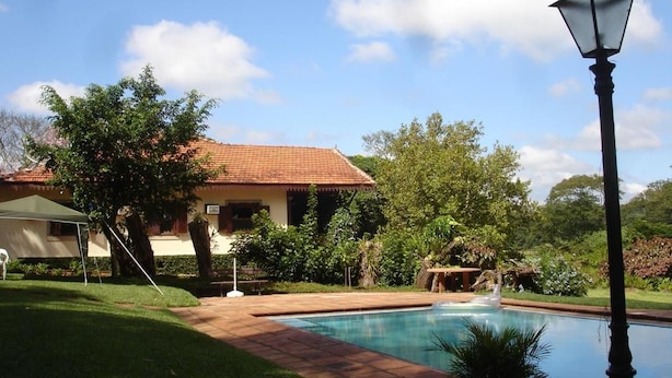 A swimming pool with a tiled deck, surrounded by a well-maintained lawn and trees. - Pousada Fazenda Pinhalzinho (Ribeirao Claro)