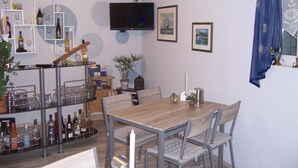 Uma sala de jantar com mesa e cadeiras de madeira, televisão fixada na parede e um espaço de bar com prateleiras cheias de garrafas e copos.