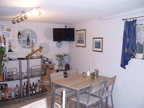 A dining area with a wooden table and chairs, a television mounted on the wall, and a bar area with shelves of bottles and glasses. - Gästehaus Schneider (Bechtheim)