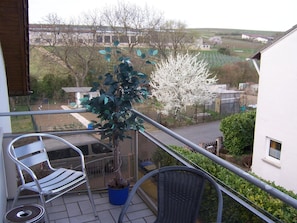 A balcony with a chair, a potted plant, and a view of a rural landscape. - Gästehaus Schneider (Bechtheim)