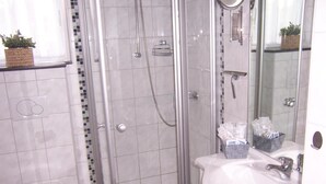Casa de banho com cabine de chuveiro em vidro, sanita e lavatório com espelho.