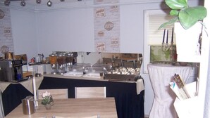 Disposição de buffet com diversas estações de comida, um bar de café e uma área de refeições com mesas e cadeiras.