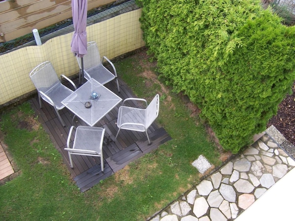 A patio with a table and chairs, surrounded by a hedge and a stone wall. - Gästehaus Schneider (Bechtheim)