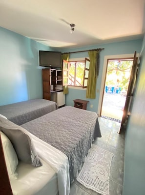 Quarto com duas camas, televisão, um pequeno armário e porta que dá para área externa com cadeiras.
