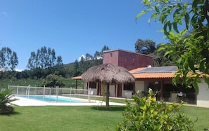 A house with a swimming pool, a thatched roof, and a fenced yard. - Pousada Tia Tuquinha (Piumhi)