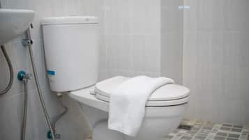 Un water bianco con un asciugamano sul coperchio, serbatoio a vista e doccetta.