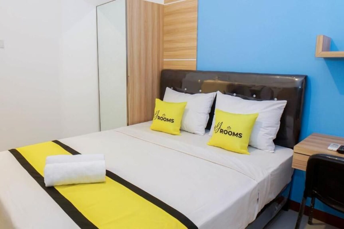 A hotel room with a bed, a bedside table, a chair, and a wardrobe.
