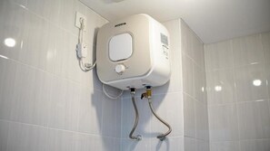 Ein an der Wand montierter Boiler mit Drehregler, verbunden mit einem flexiblen Schlauch und einem Wandventil.
