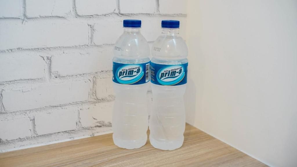 Two bottles of air mineral water on a wooden surface against a white brick wall.