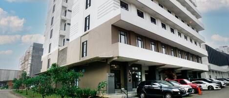 A multi-story hotel with a modern design, featuring a covered entrance and a parking area with several cars.