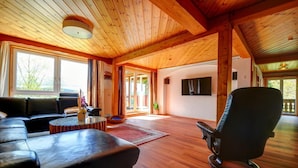 A spacious living room with a wooden ceiling, a black leather sofa, a round coffee table, and a black armchair. - Feriendomizil Schwarzwald (Feldberg)