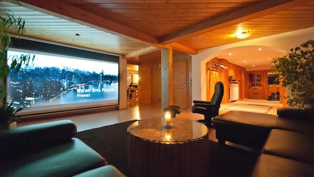 A modern living room with a large television displaying a cityscape, a round coffee table, leather sofas, and a wooden ceiling. - Feriendomizil Schwarzwald (Feldberg)