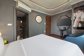 A hotel room with a bed, a shower, a vanity with a mirror, and a robe hanging on a hook. - Premium Madelis Hotel (Hanoi)