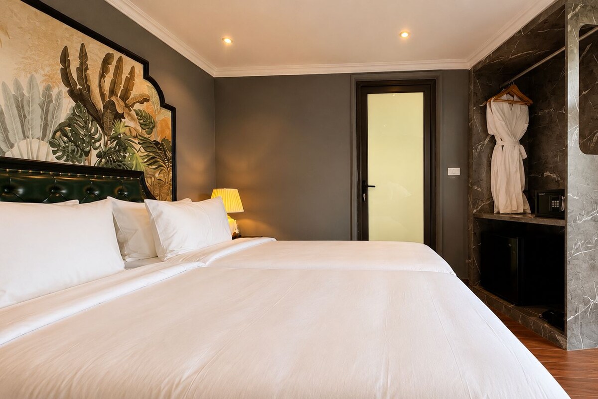 Habitación de hotel con una cama grande, una mesita de noche, una lámpara, una bata colgada en un perchero y una puerta que da a otra habitación.