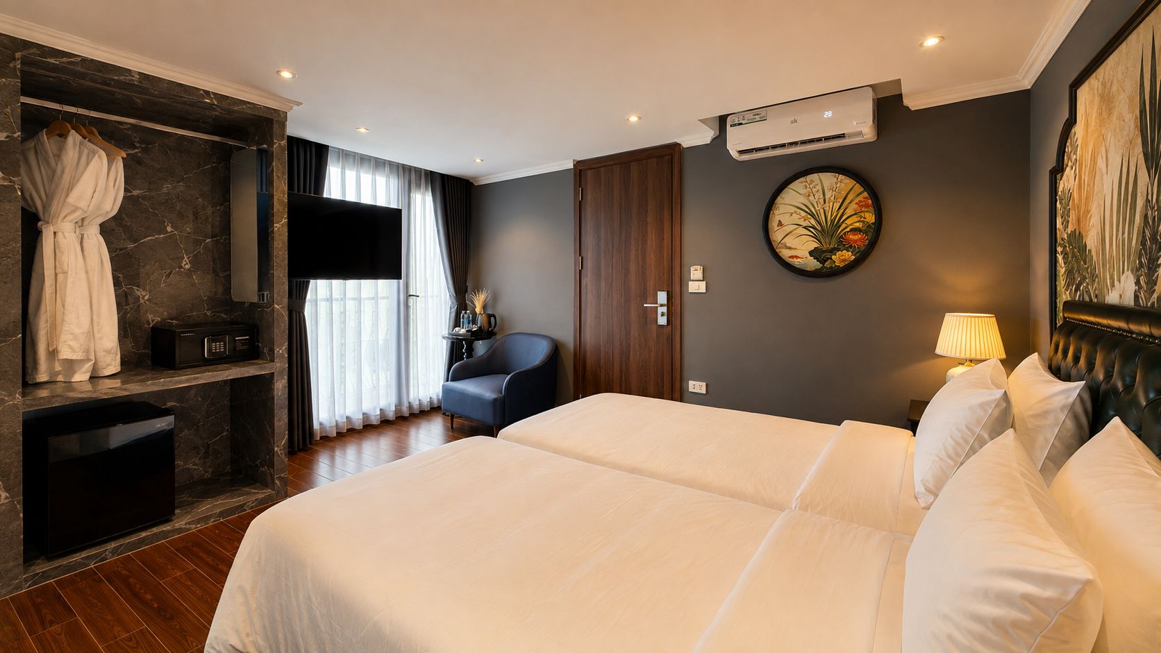 Ein Hotelzimmer mit einem großen Bett, einer Sitzecke mit einem Sessel, einem Flachbildfernseher, einem kleinen Tisch mit einer Vase und einer Wandklimaanlage.