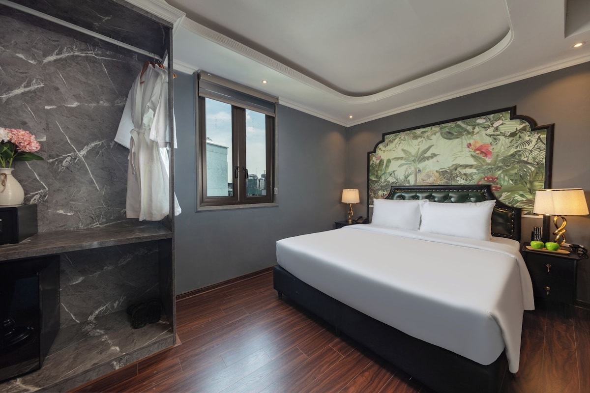 Habitación de hotel con una cama grande, cabecera con diseño floral, pared de mármol y ventana con vista a la ciudad.