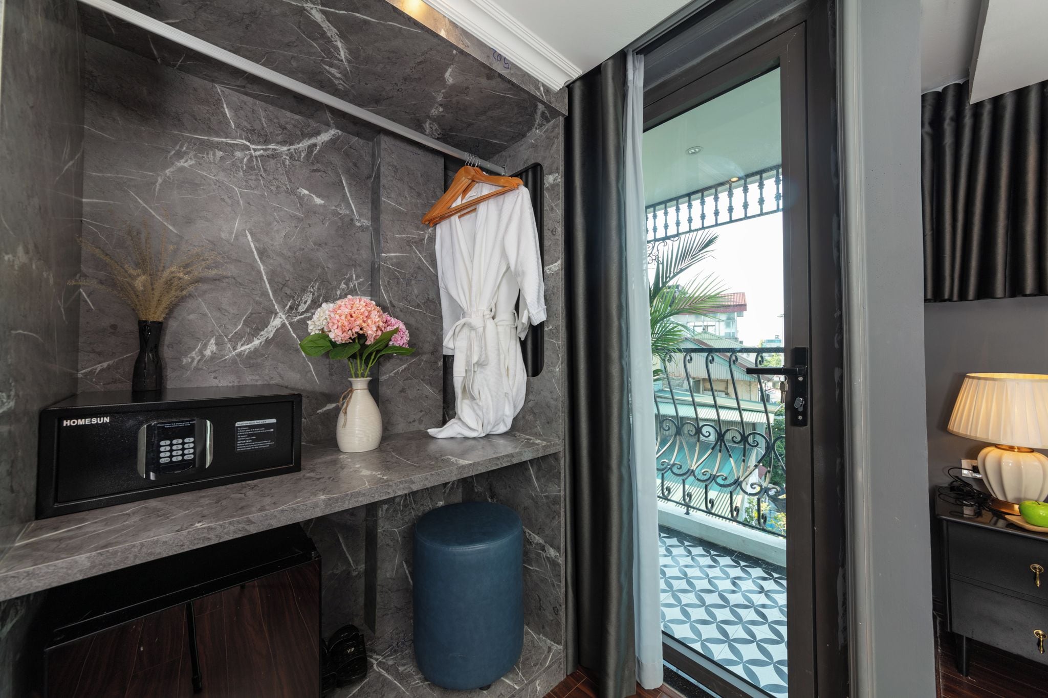 Casa de banho com parede de mármore, micro-ondas preto, um vaso com flores e um roupão pendurado.
