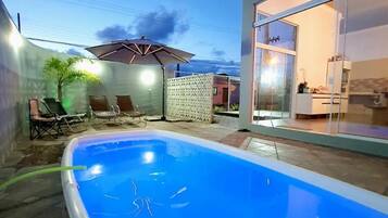 Piscina com superfície de água azul e límpida, cercada por um espaço de terraço com mobiliário de exterior.