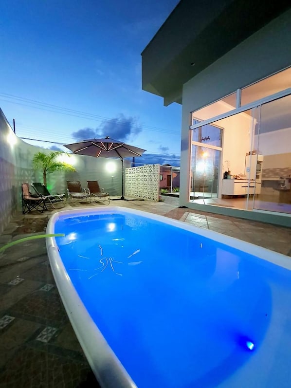 A swimming pool with a clear blue water surface, surrounded by a patio area with outdoor furniture. - Pousada Solari (São Francisco do Sul)