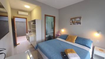 Quarto de hotel com cama, mesa de cabeceira e escrivaninha.