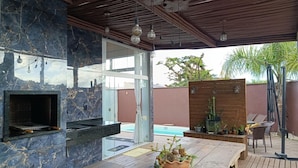 Um pátio ao ar livre com churrasqueira, piscina e um deck de madeira com cadeiras.