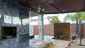 An outdoor patio with a built-in grill, a pool, and a wooden deck with chairs. - Pousada Solari (São Francisco do Sul)