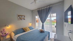 Quarto com cama, mesa de cabeceira, televisão na parede e ventilador de teto.