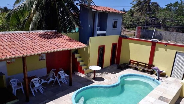A swimming pool with a red roofed area and white chairs. - Top Home Pousada (Caucaia)